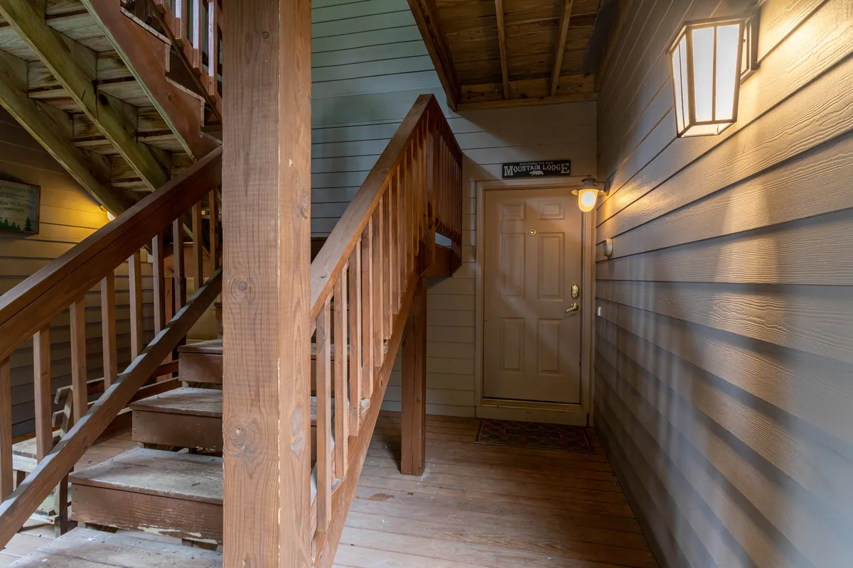 An interior view of the building's common area shows a sturdy staircase, front door, and an outdoor light fixture. This space is where guests access their units, emphasizing the entry process and the lower-level setting mentioned in the section.