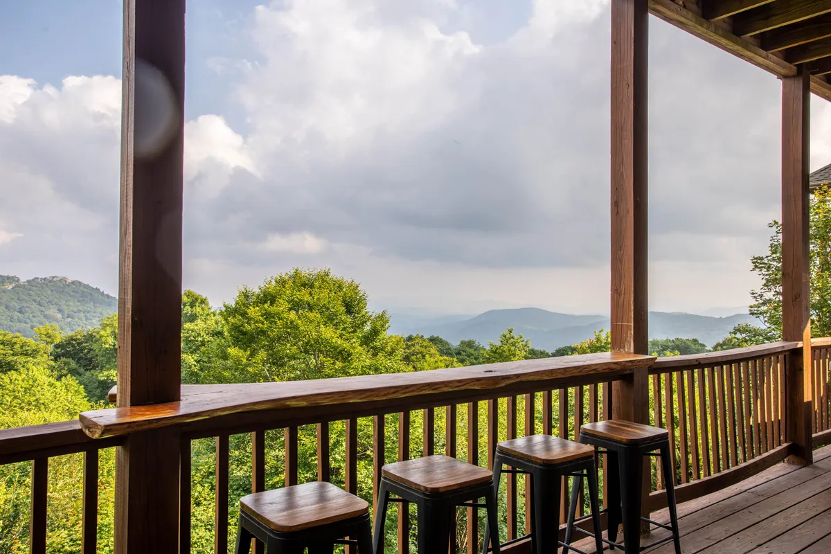 A scenic exterior shot from the balcony or deck, showcasing wooden railings, stools, and a sweeping view of the mountains. The atmosphere is relaxed, suggesting a perfect spot to unwind after a day on the slopes.