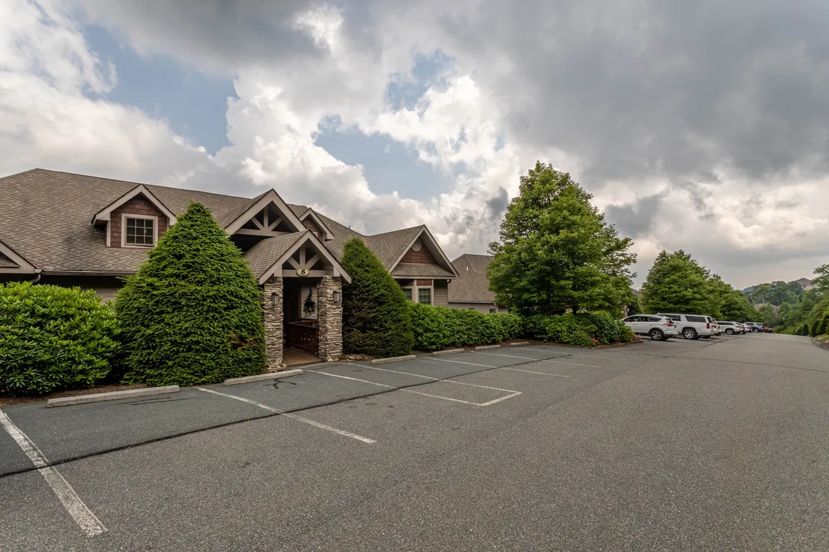 This exterior image features a stone entrance flanked by landscaped bushes, with an adjacent parking area visible. The well-maintained entry and clear parking access reflect the managed aspect of the Reserve community and show the type of arrival experience guests can expect.