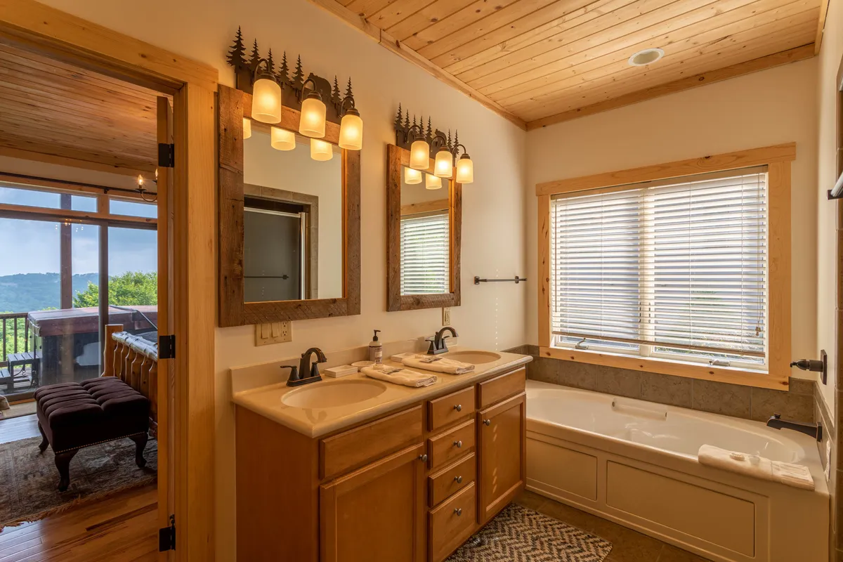 A luxurious bathroom with a double sink vanity, a spacious bathtub, a mirrored wall enhanced by soft lighting, and a window offering views and natural light. The atmosphere is serene and inviting, perfect for unwinding after a day of adventure.