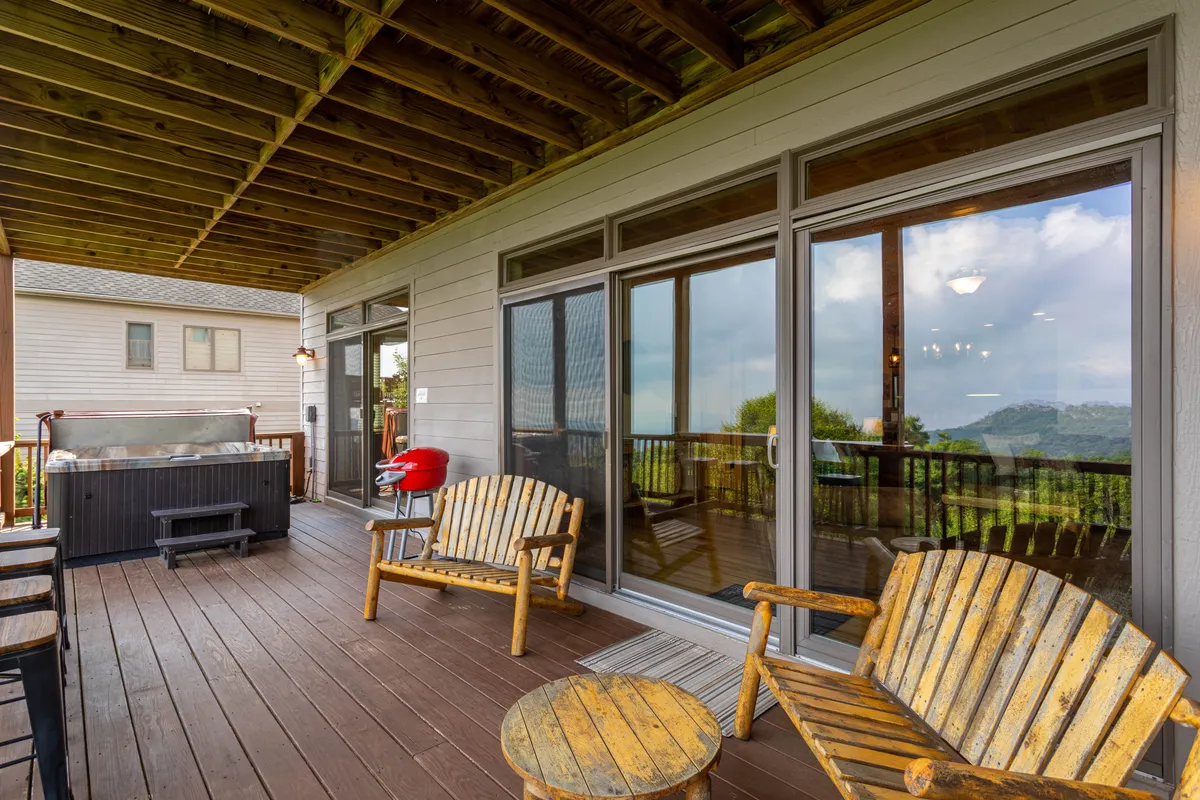 The deck is shown with wooden chairs and a hot tub positioned for optimal mountain viewing. Glass doors connect the deck to the interior, while the expansive vistas evoke tranquility and the promise of both sunrise and starlit evenings.